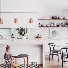 a woman sitting at a kitchen table with a child in front of her on a laptop