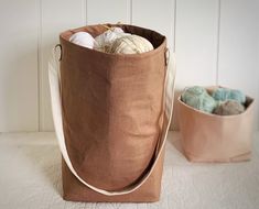 a brown bag sitting next to a white bowl filled with balls of yarn