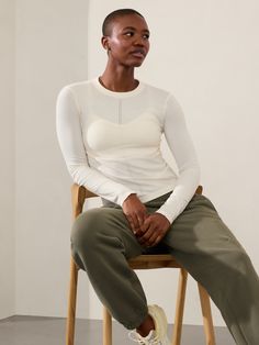 a woman sitting on top of a wooden chair wearing white shirt and khaki pants