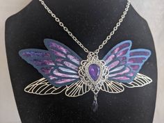 This gorgeous necklace features purple, black, and silver fairy wings with a opalescent purple gem in the middle. A drop crystal hangs from the center.  Perfect for special occasions or to add a bit of magic to your everyday! Handmade Purple Fantasy Necklaces, Handmade Purple Fantasy Necklace, Purple Fantasy Necklace For Gift, Fantasy Style Purple Necklace For Gift, Magical Purple Pendant Necklace, Faerie Wedding, Magical Aesthetic, Silver Fairy, Purple Fairy