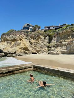 two people are swimming in the water near some cliffs and houses on top of a cliff