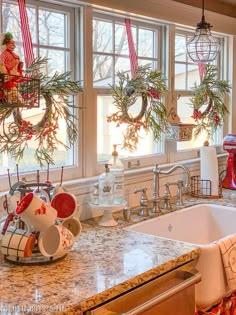 a kitchen decorated for christmas with wreaths hanging from the windows