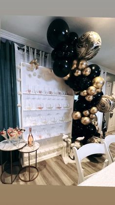 black and gold balloons are hanging from the ceiling in a room with white walls, chairs and tables