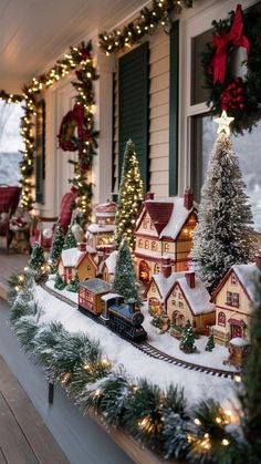 christmas decorations on the front porch of a house with trees and lights around it, along with a train