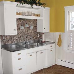 a kitchen with yellow walls and white cupboards, stainless steel sink and tile backsplash