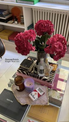 pink flowers in a vase sitting on top of a table next to books and magazines