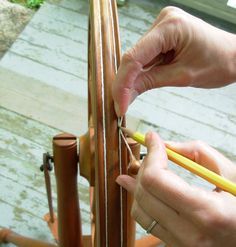 a person is holding a pencil and stringing the top of a wooden chair with wood slats