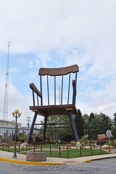 a large wooden chair sitting on the side of a road next to a street light