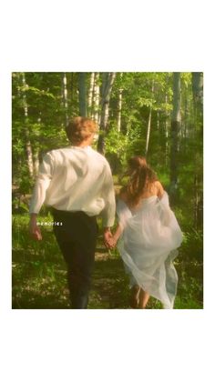 a man and woman are walking through the woods together, holding hands with each other