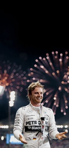 a man standing on top of a field with fireworks in the sky behind him and holding his hands out