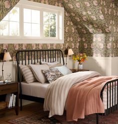 a bed sitting in a bedroom next to a window with flowers on the wall behind it