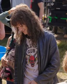 a man with long hair wearing a leather jacket and standing in front of other people