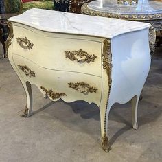 an ornate white and gold painted chest of drawers with glass top, on display in a store