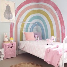 a child's bedroom decorated in pastel pink, blue and yellow with a rainbow painted on the wall