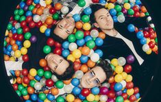 two men in a ball pit surrounded by balloons and confetti, with one man looking at the camera