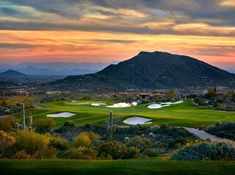 a golf course with mountains in the background and clouds above it at sunset or sunrise