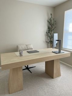 a table with a laptop on it in front of a window and a plant next to it