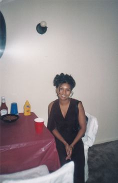 a woman sitting in front of a red table with drinks on it and an object hanging from the wall behind her