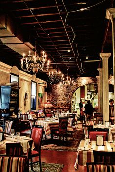 a restaurant with many tables and chairs, chandeliers hanging from the ceiling over them