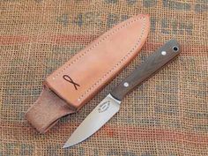 a knife and sheath sitting on top of a cloth covered tablecloth with a brown leather case