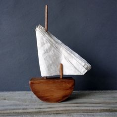 a small sailboat made out of wood and paper towels on a wooden stand against a blue wall