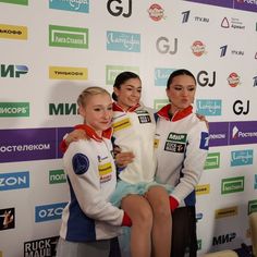 three women sitting on top of each other in front of a wall