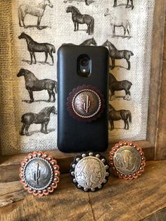 three different types of horse brooches are sitting on a wooden shelf next to a cell phone