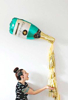 a woman is pouring champagne into a wine bottle shaped like a balloon with streamers attached to it