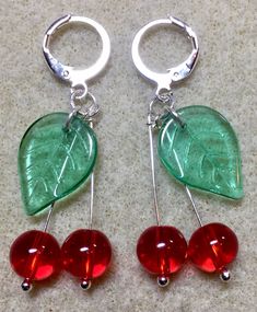 two red and green cherries are hanging from silver hoop earrings on a white surface