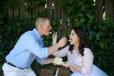 a man feeding a woman cake while sitting on a bench in front of greenery