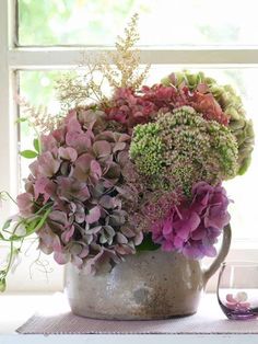 a vase filled with purple and green flowers on top of a table next to a window