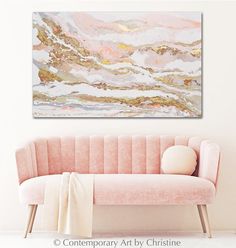 a pink couch sitting in front of a white wall with a painting on the wall