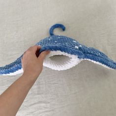 a hand is holding a blue and white crocheted umbrella on a white sheet