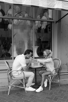 a man and woman sitting at a table in front of a store window playing with each other