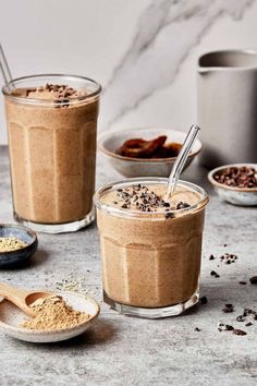 two glasses filled with chocolate pudding on top of a table next to bowls and spoons