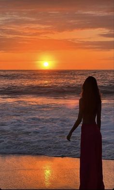 a woman standing on top of a sandy beach next to the ocean at sunset or dawn