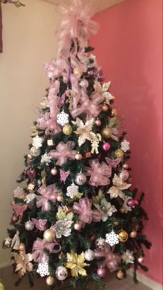 a decorated christmas tree with pink and gold ornaments on it's base, against a pink wall