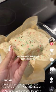 someone holding up a piece of cake in front of an oven with white frosting and sprinkles