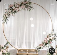 a wedding arch decorated with pink flowers and greenery in front of a white curtain