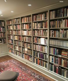 a living room filled with lots of books on top of a book shelf next to a rug