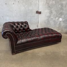 a brown leather chaise lounger sitting in front of a concrete wall and cement floor