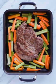 a roasting pan with carrots, celery and meat in it on a marble surface