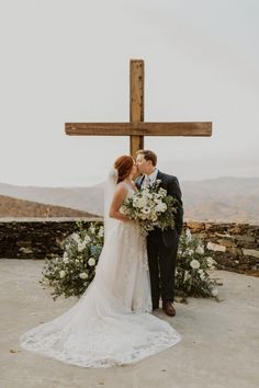 a bride and groom kissing in front of a cross