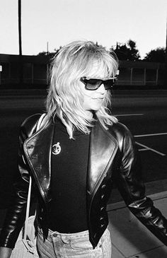 black and white photograph of woman in leather jacket walking down the street with handbag