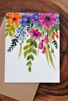 a card with watercolor flowers on it sitting on top of a piece of wood