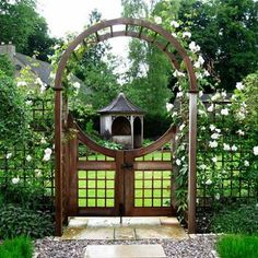 a wooden gate surrounded by white flowers and greenery with a gazebo in the background