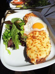 an egg and cheese sandwich on a white plate with a green salad next to it