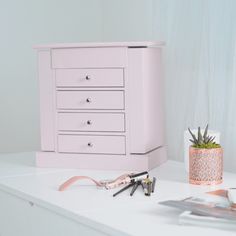 a white dresser sitting on top of a table next to a potted plant and scissors