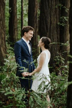 a bride and groom standing in the middle of a forest looking into each other's eyes