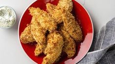 a red plate topped with fried chicken next to a small bowl of ranch dips